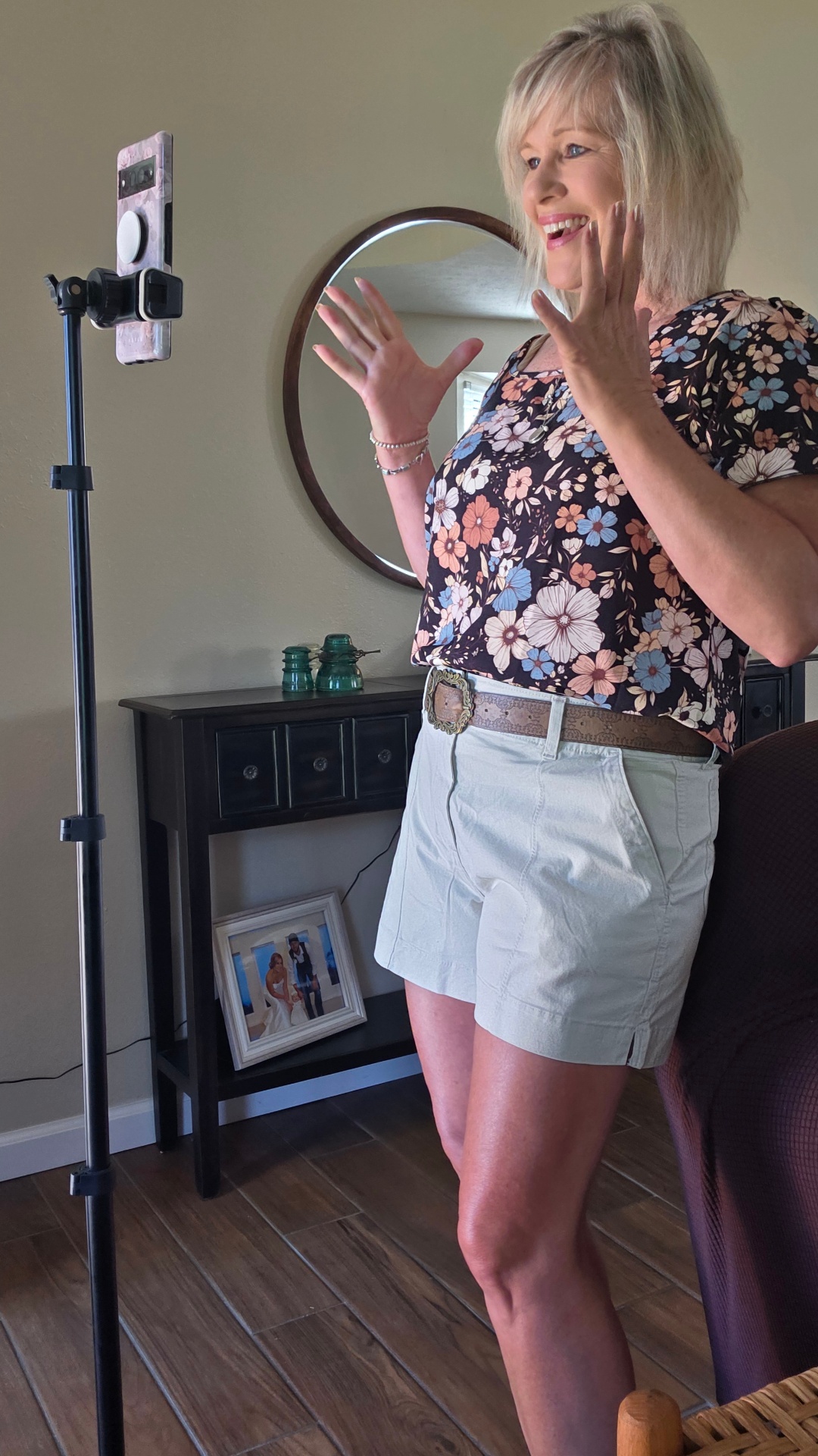 Alica Rutherford filming UGC content with a smartphone on a tripod, smiling and gesturing on camera in a home setting.