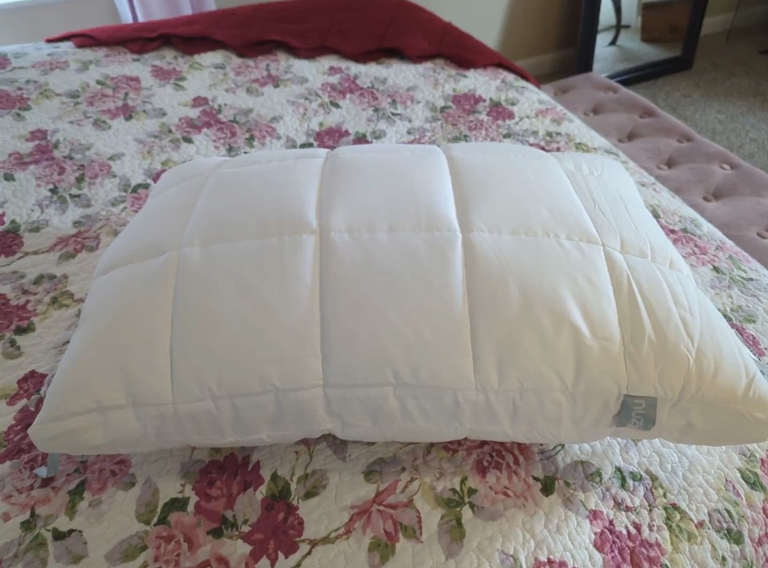 Nuzzle pillow displayed on a floral quilted bed, showcasing its plush quilted construction.