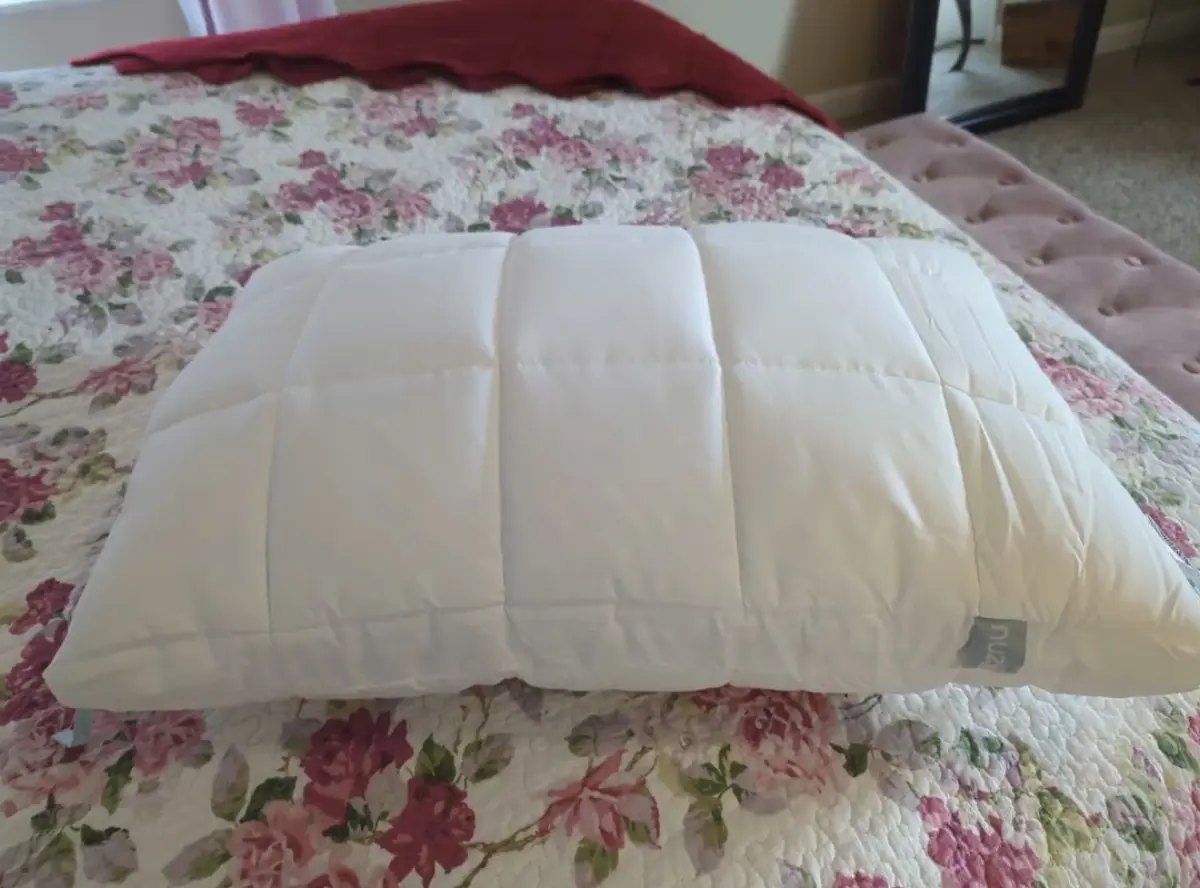 Nuzzle pillow displayed on a floral quilted bed, showcasing its plush quilted construction.